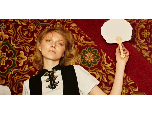 White female model lying on rug holding a fan