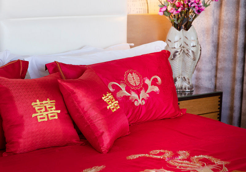 A bed set up with red double happiness pillows and bed spread
