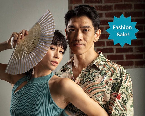 Woman holding white fan and wearing a blue sleeveless top. Man wearing a crane design collared shirt