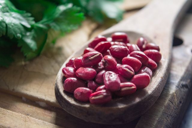 Adzuki beans on a wooden spoon beside a sprig of green herbs