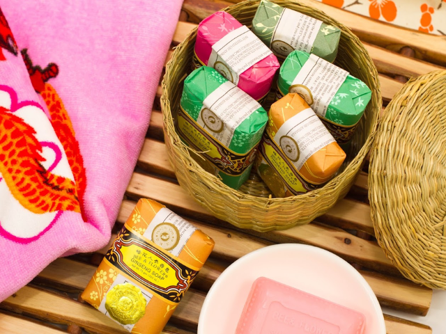 Basket of Bee & Flower brand soap next to pink towel on wooden board