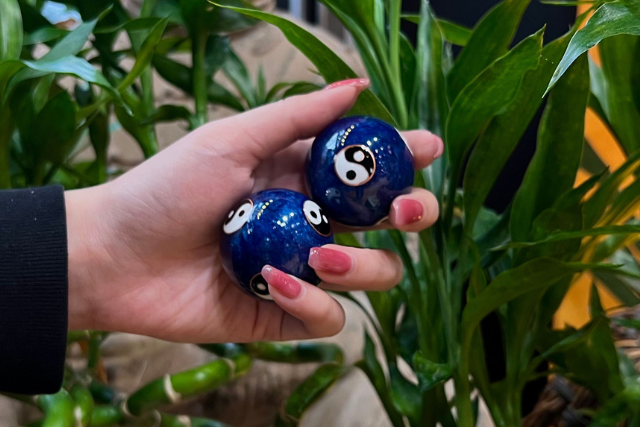 Someone holding pair of blue Chinese therapy balls with yin yang design