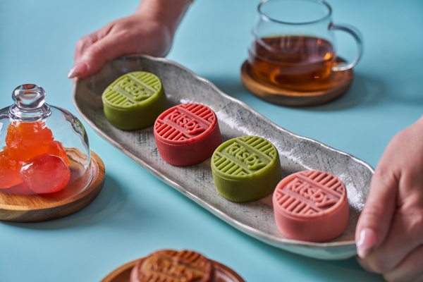 Four Kitsby mooncakes in pink and green on a long dish being held by a person