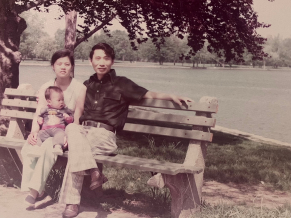 A couple with an infant sitting on a bench by a river