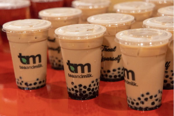 Cups with bubble tea and Tea and Milk logo on red table