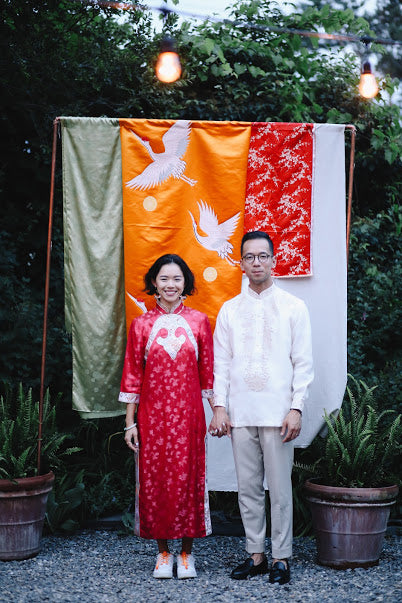 Vicki Ho and husband Todd at wedding in front of traditional Chinese brocades