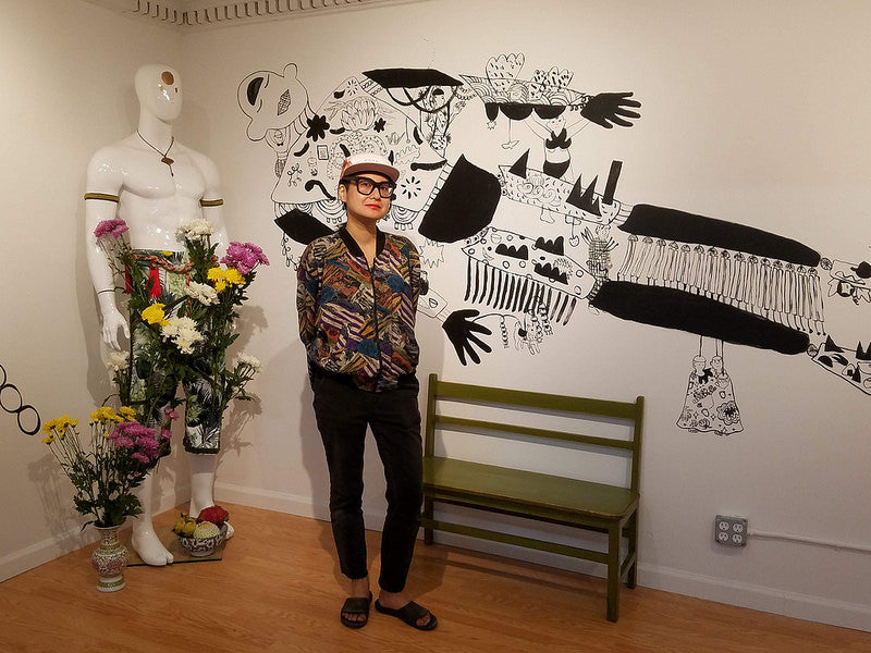 Artist Yumi Sakugawa in front of her mural and mannequin with flowers in the Pearl River Mart gallery