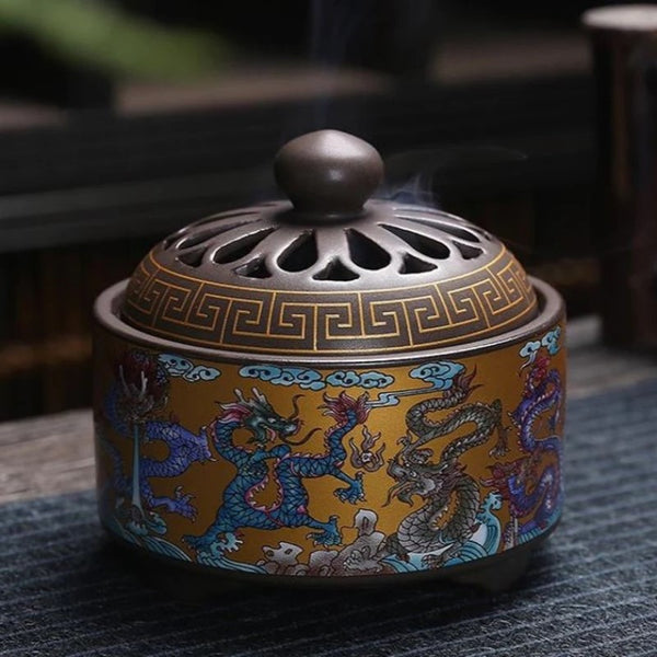 Round Enamel Incense Burner with dragon design on a golden yellow background. Smoke from an incense cone is emitted through the holes of the lid.