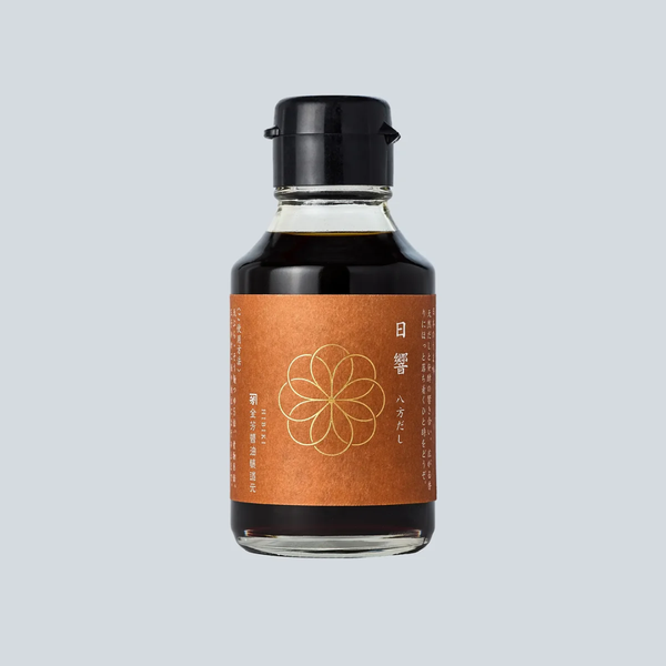 A small glass bottle of dark soy sauce with a black cap and a copper-brown label featuring a gold floral design and Japanese text, centered on a light gray background.