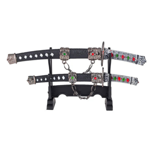 Two black leather harness straps with silver buckles, studs, and red-and-green accents rest on a stand, linked by chains