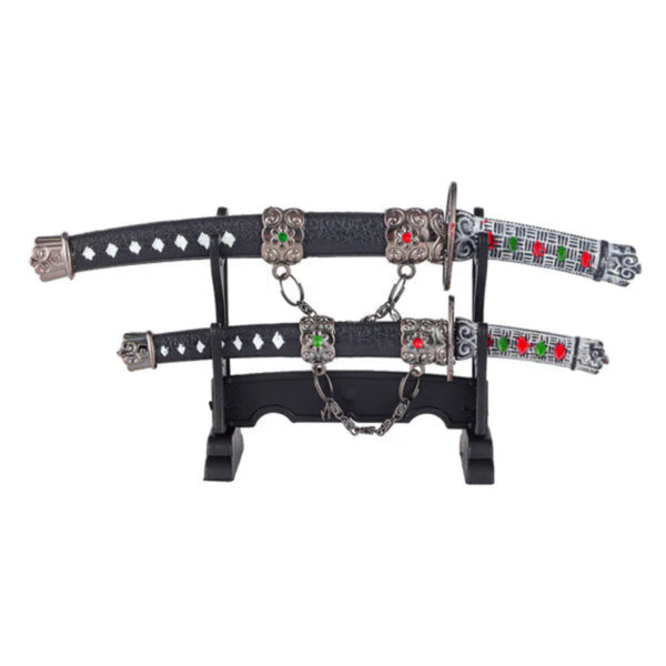 Two black leather harness straps with silver buckles, studs, and red-and-green accents rest on a stand, linked by chains