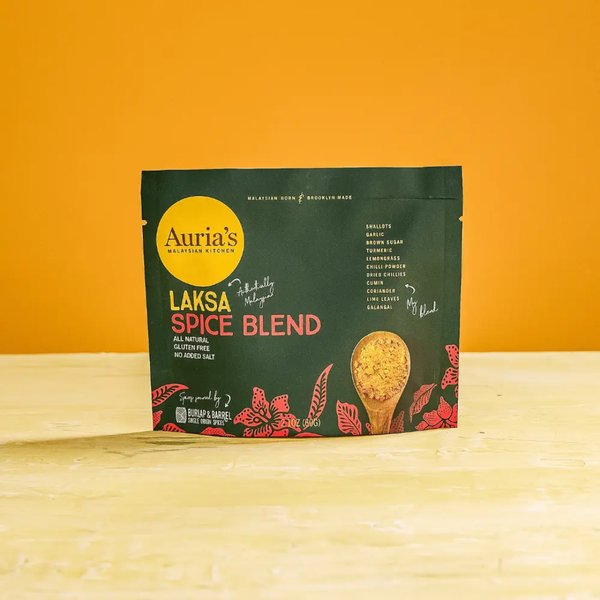 Auria's Laksa Spice Blend package on a wooden surface with an orange background