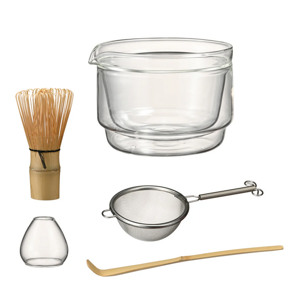 Set of tea-making tools including a whisk, glass bowl, strainer, and other utensils on a white background