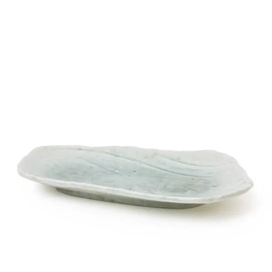 A small, irregularly shaped ceramic dish with a pale sage green glaze, photographed on a seamless white background.