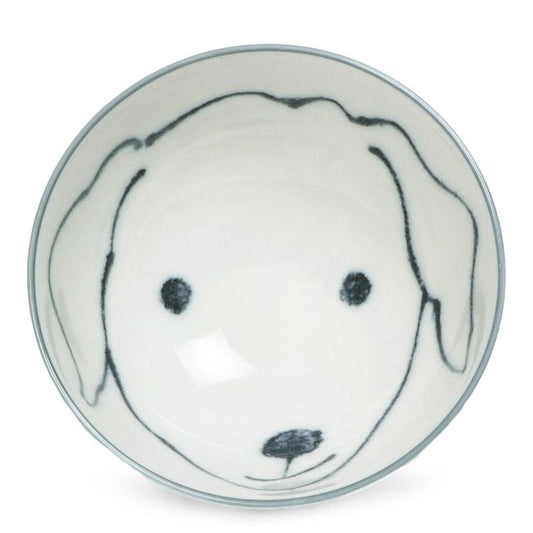 A white ceramic bowl with a minimalist dog face design, featuring simple outlines for ears and features. The tone is playful and charming.