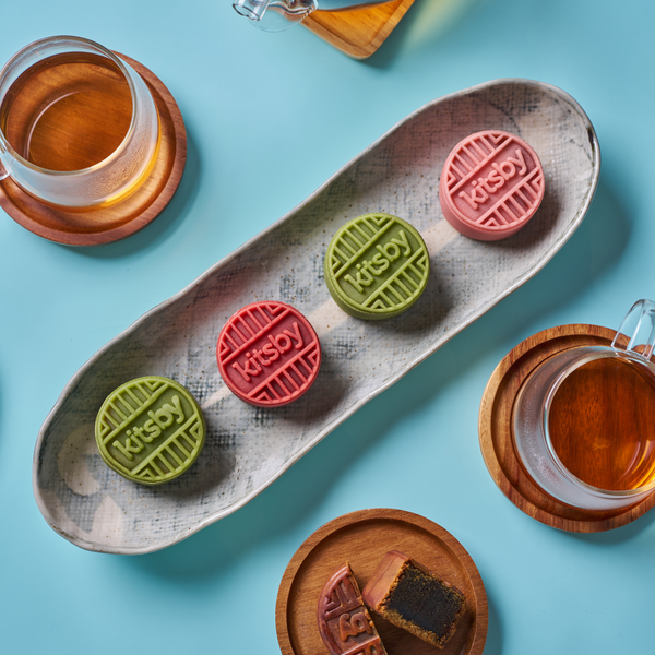 Green and pink Kitsby mooncakes on light blue-gray patterned dish