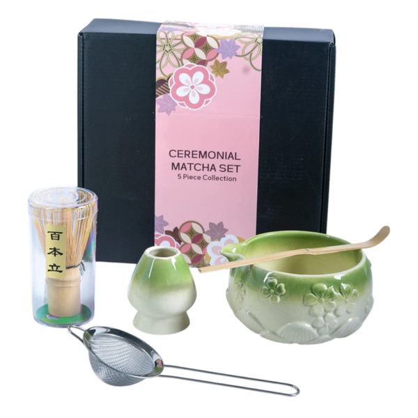 Ceremonial matcha set with green bowl, whisk, and other tools in front of a decorative box.
