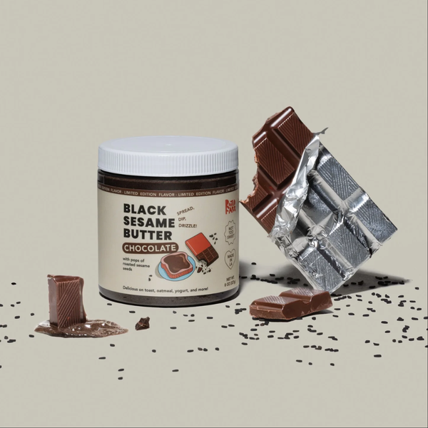 Jar of Black Sesame Butter Chocolate beside chocolate bar with bite out of it on gray background