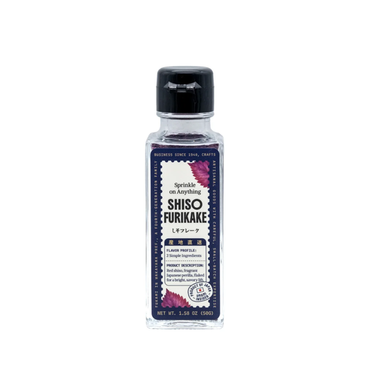 A bottle of Shiso Furikake seasoning by The Art of Seasoning, featuring a clear glass bottle with a black cap and a dark purple label decorated with pink shiso leaves.