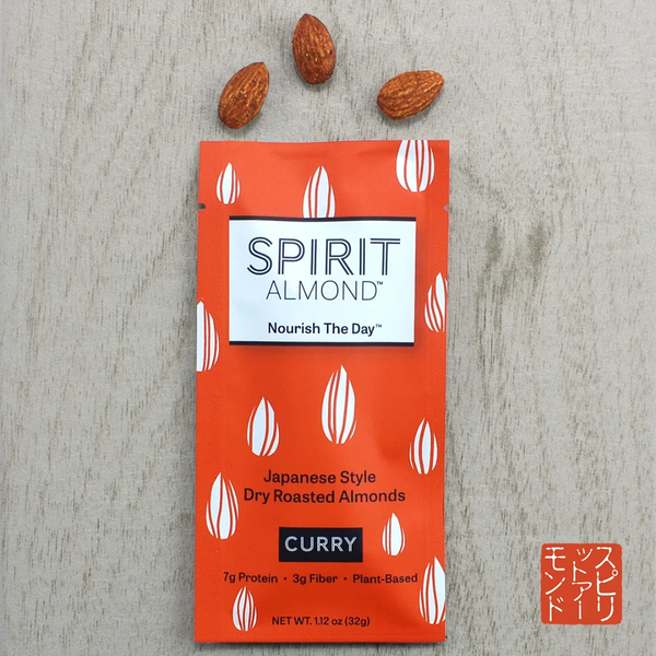 A package of Spirit Almond Curry flavor dry roasted almonds on a light gray textured background, with three whole almonds placed above the package.