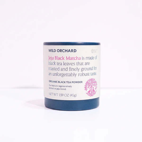 Wild Orchard Jeju Black Matcha organic black tea powder in a cylindrical white jar with a dark blue lid and base, set against a plain white background.