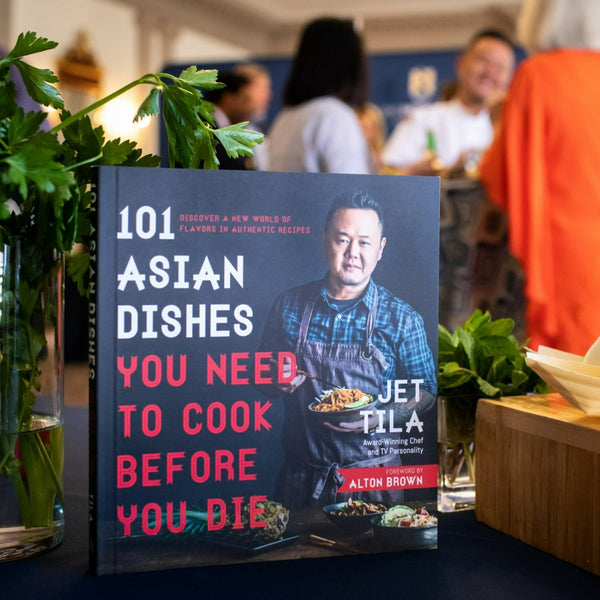 Jet Tila's Book standing on a table with the chef out of focus in the background speaking with guests