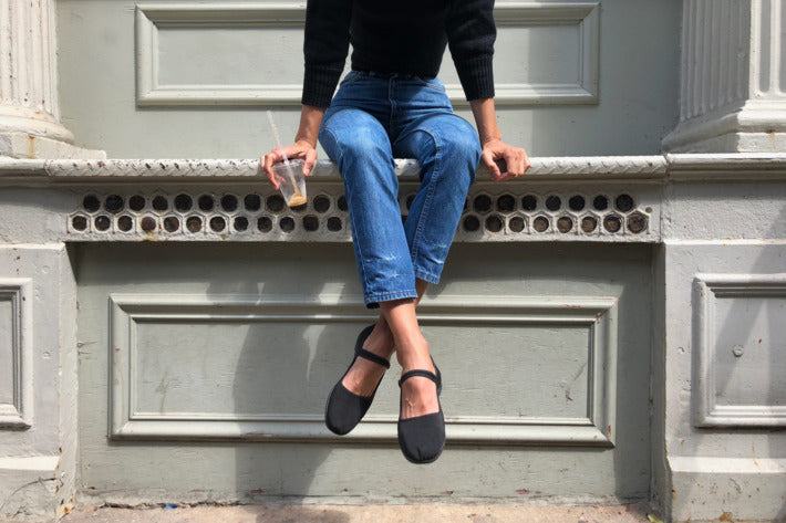 Sitting woman in jeans and black sweater wearing black Mary Jane shoes