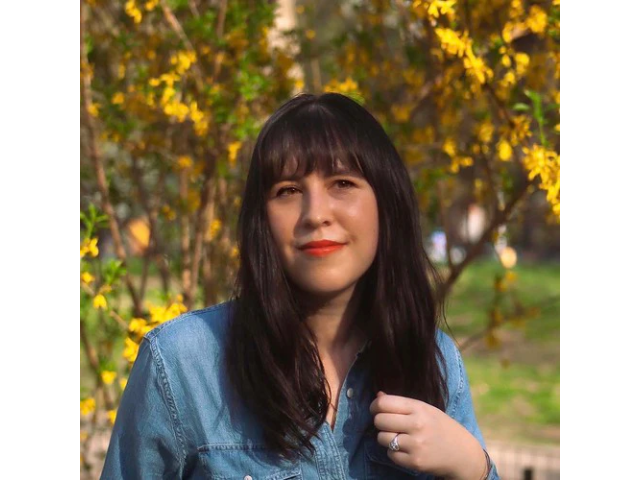 Woman with dark hair and blue shirt standing in front of tree