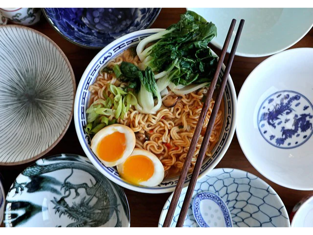 Noodles with an egg and bok choy in a bowl with chopsticks surrounded by blue and white bowls