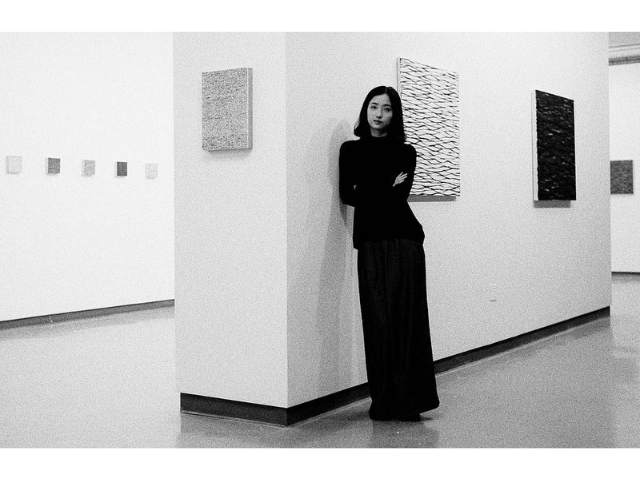 Artist Yingqian Cao in long black dress in art gallery with her work