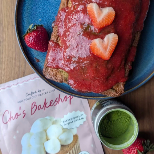 Cake with strawberry sauce and slices on blue plate beside package of Cho's Bakeshop mix and green cup