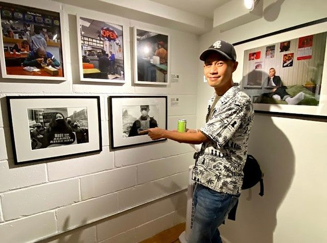 Photographer Edward Cheng pointing at his photographs in the Pearl River Mart Soho gallery