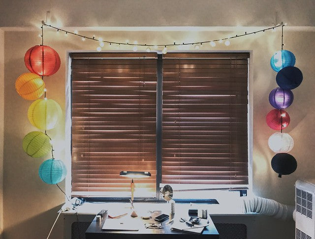 Window with drawn blinds surrounded by colorful lanterns and string lights