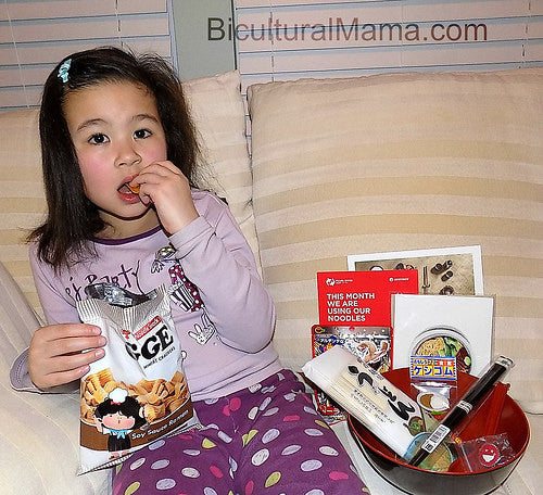 Little girl eating snacks next to items from Pearl River Mart noodle Friendship Box