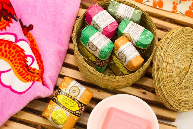 Various Bee and Flower soaps in a smal basket beside a pink towel with dragon design