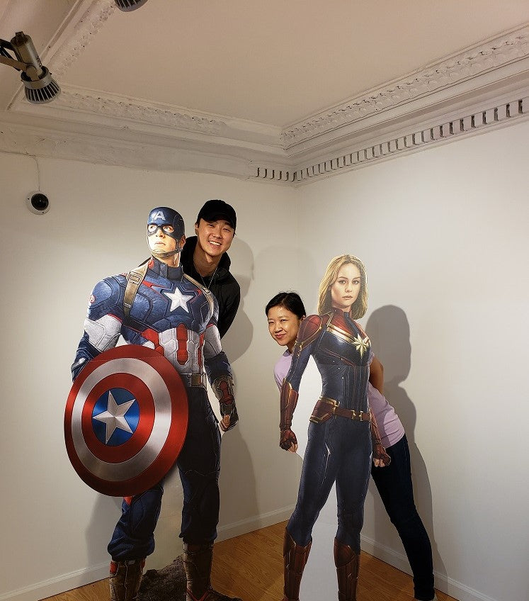 The artist William Yu and Pearl River President Joanne Kwong posing with cardboard cutouts of Captains America and Marvel