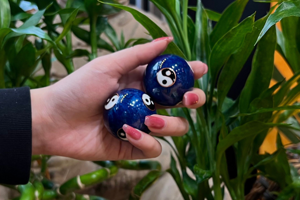 Someone holding pair of blue Chinese therapy balls with yin yang design