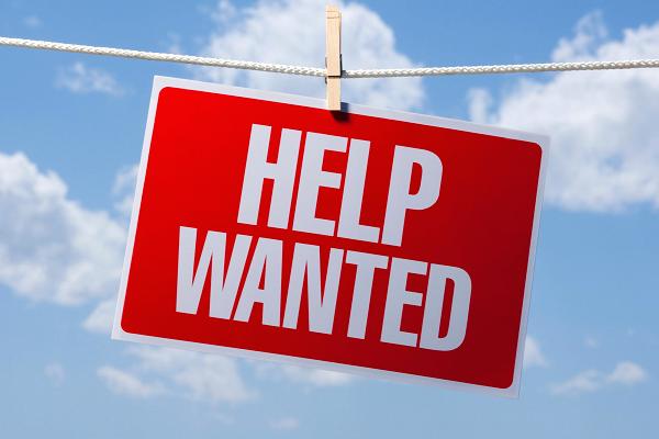 Red Help Wanted sign hanging on clothesline in front of blue sky