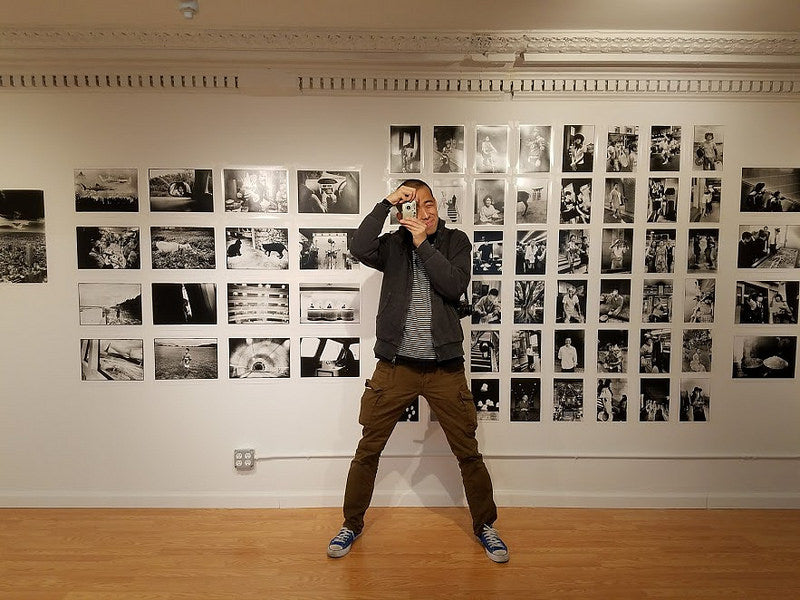 Photographer Hiro Ito with his camera in front of his photographs at the Pearl River Mart gallery