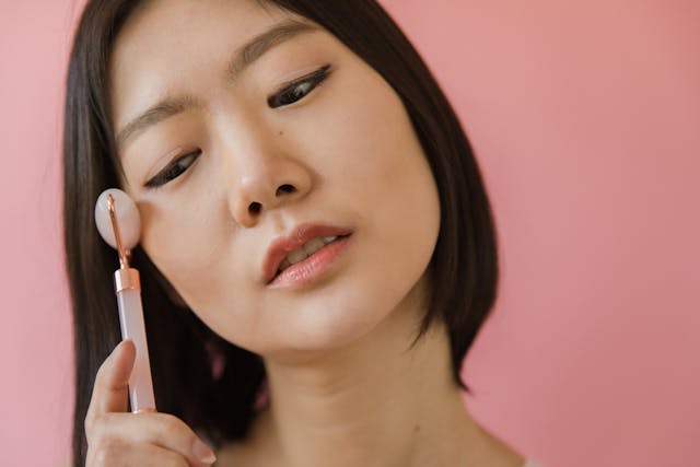 Woman using pink jade roller against pink background