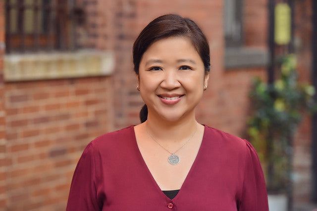 Joanne Kwong in burgundy shirt in front of brick wall