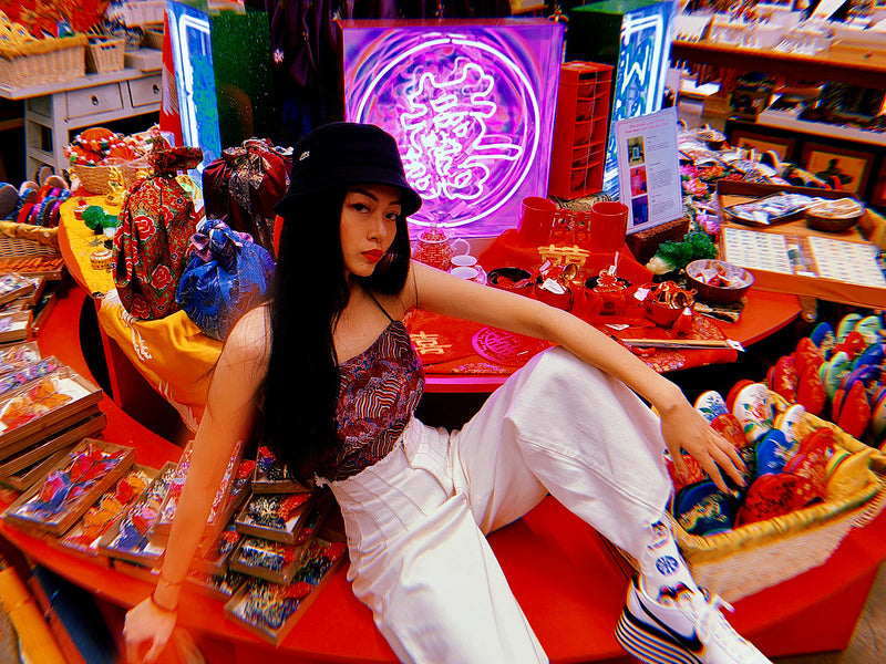 Neon sculpture artist Juno Shen lounging on display in front of her mahjong light piece at Pearl River Mart in Chelsea Market