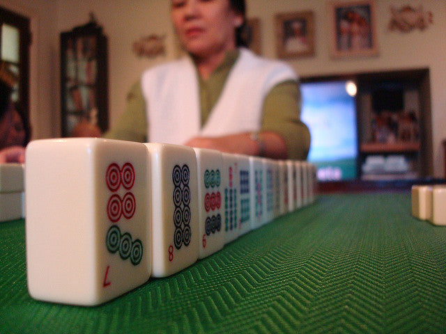 A row of mahjongg tiles on a green table with a lady in the background