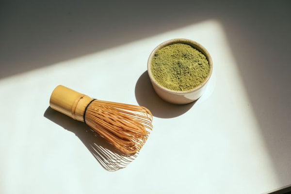 Small cup of matcha powder beside matcha whisk