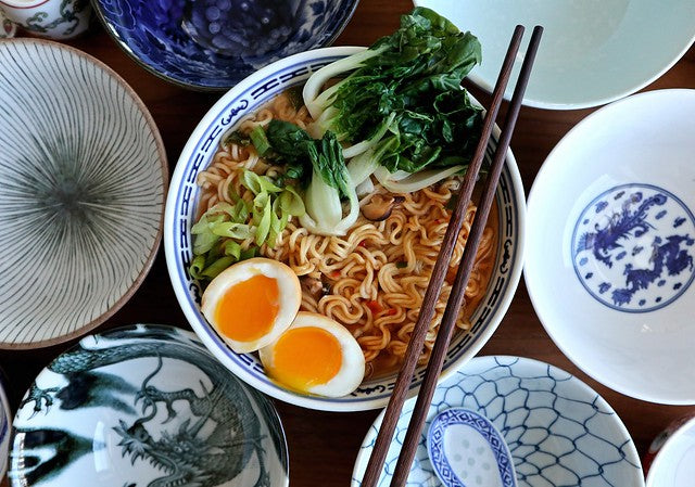 Noodles with an egg and bok choy in a bowl with chopsticks surrounded by blue and white bowls