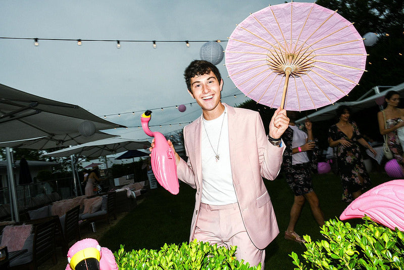 Young white man in pink suit holding pink parasol and pink flamingo