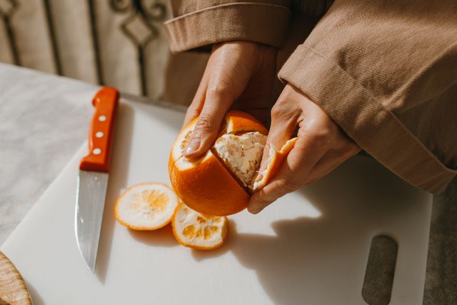 Woman peeling an orange with a cutting board and knife nearby