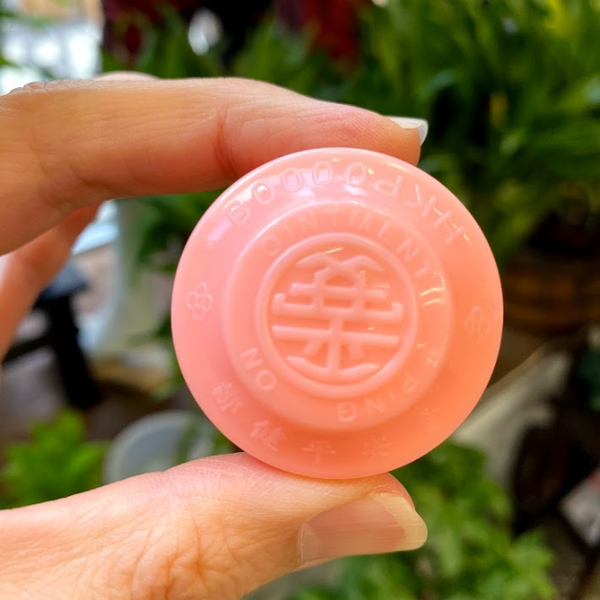 Hand holding pink jar of Ping On ointment