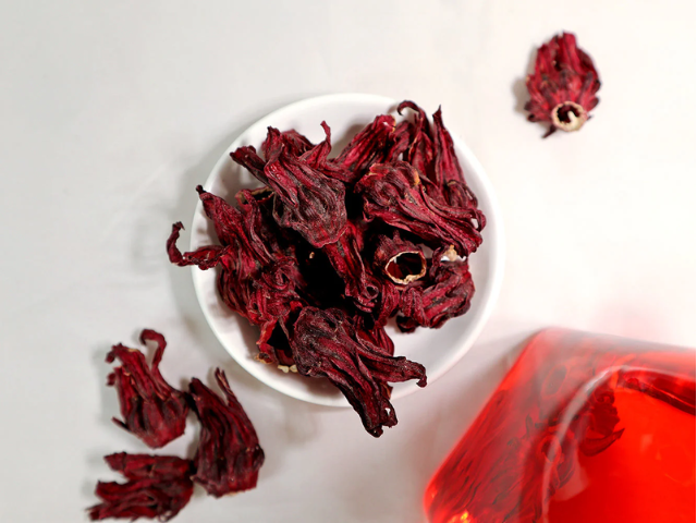 White dish with dried hibiscus petals besides glass of hibiscus tea