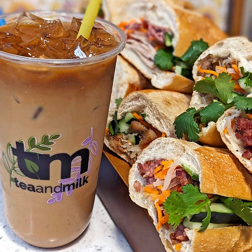 Tea and Milk Vietnamese iced coffee beside several banh mi sandwiches